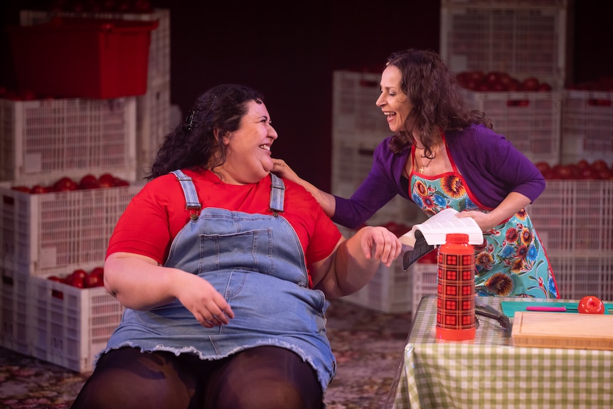 A full-figured 20-something grins at a thin middle-aged woman, wearing an apron, with her hand on the younger woman's shoulder