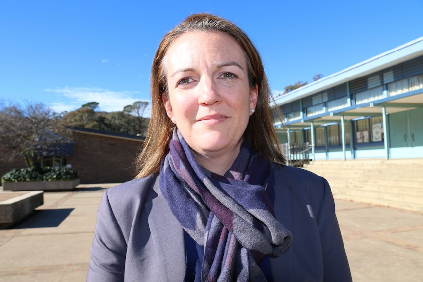 Veronica stands in school grounds looking into the camera, wearing a scarf and coat.