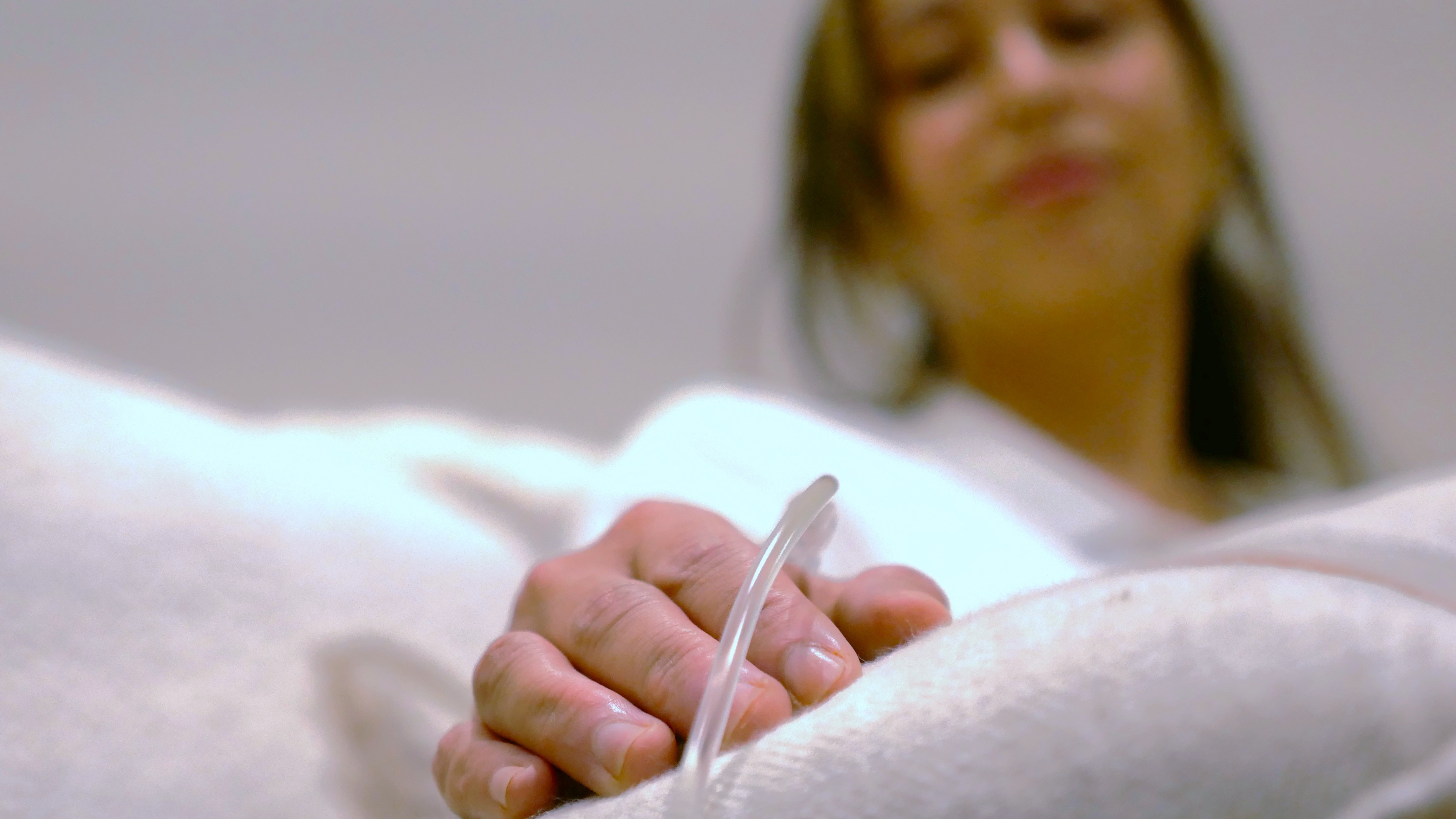 A blurred image of a woman with an IV drip in her hand.