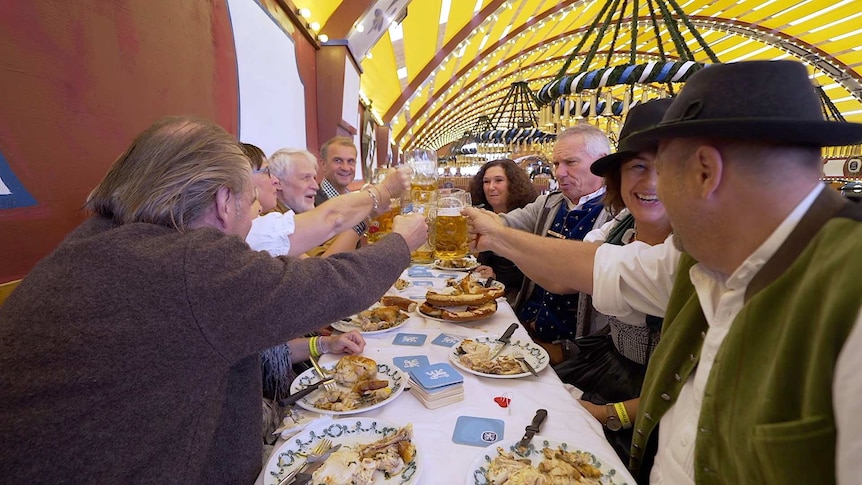 A group of people smile and clink their beers together over meals at Oktoberfest.