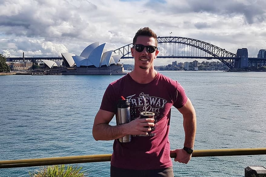 a man holding a drink standing across from Sydney harbour