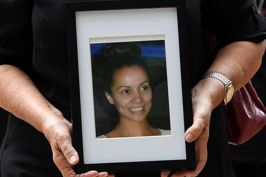 A woman holds a framed photo of murder victim Tara Brown