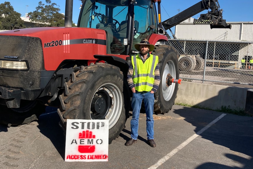 A man in farm gear and a high-vis vest stands next to a tractor with a protest placard resting against a front tyre.