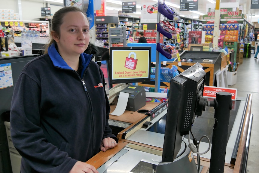 A young lady stands at a cash register in a supermarket.