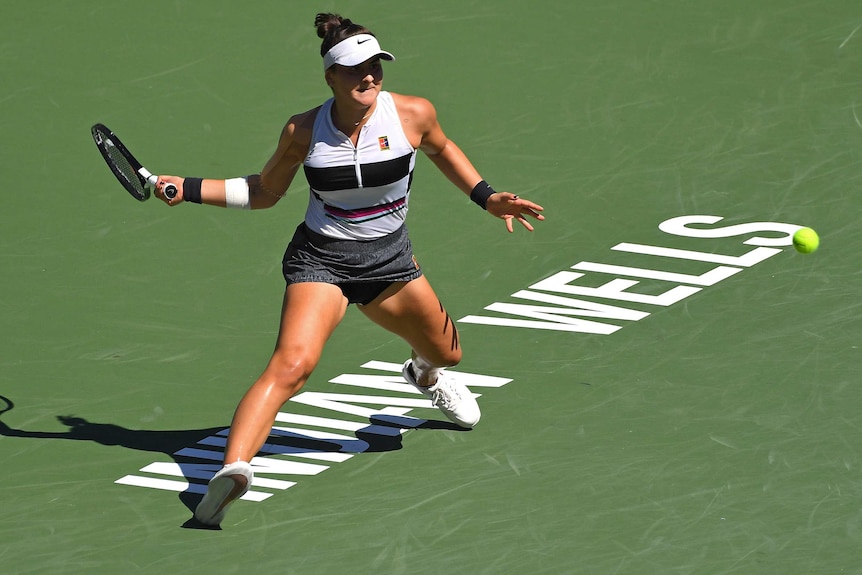 A female tennis player prepares to hit a forehand as she runs across the Indian Wells sign on the court.