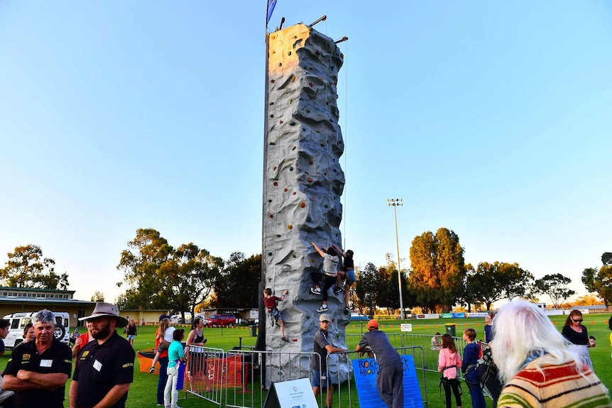 A climbing tower with people making their way up it on an oval with people standing around.