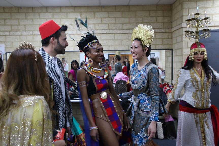 A group of models from diverse backgrounds and dressed in various outfits gather backstage at a fashion show.