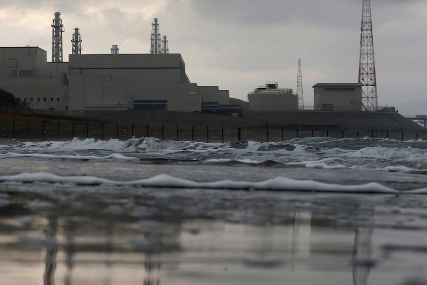 a power plant from the seaside with ocean in the foreground on an overcast day