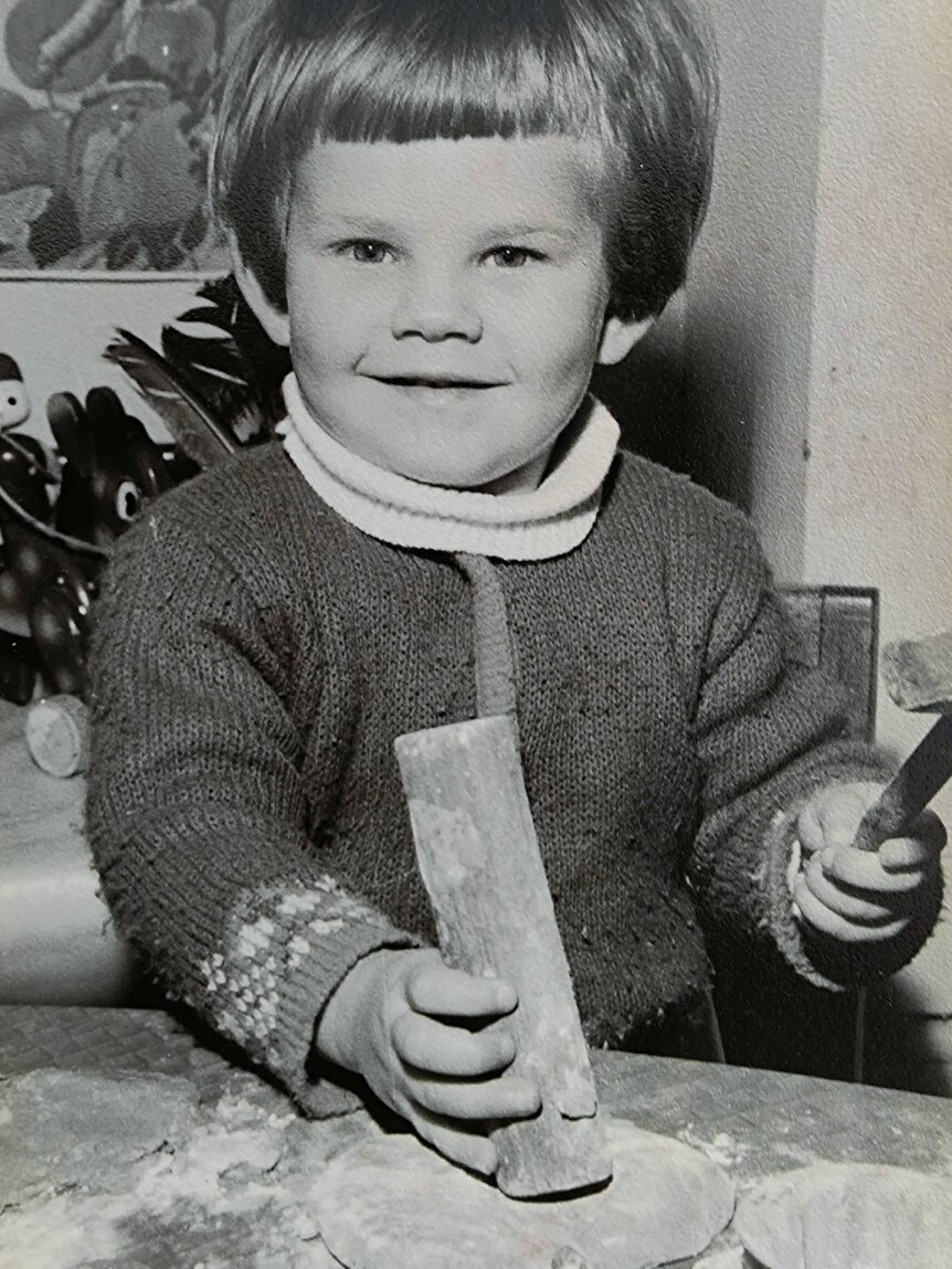 Black and white photo of a young child with a bowl haircut, playing with blocks.