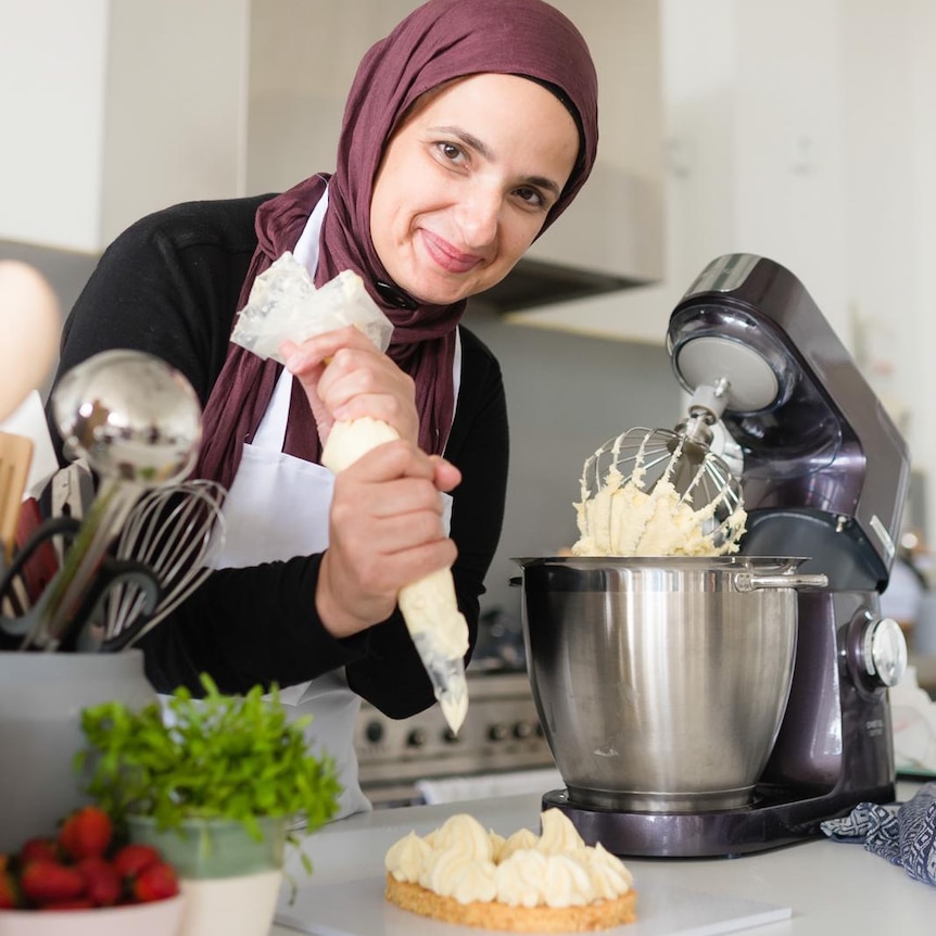 Fatimah pipes cream onto her baking in a kitchen.