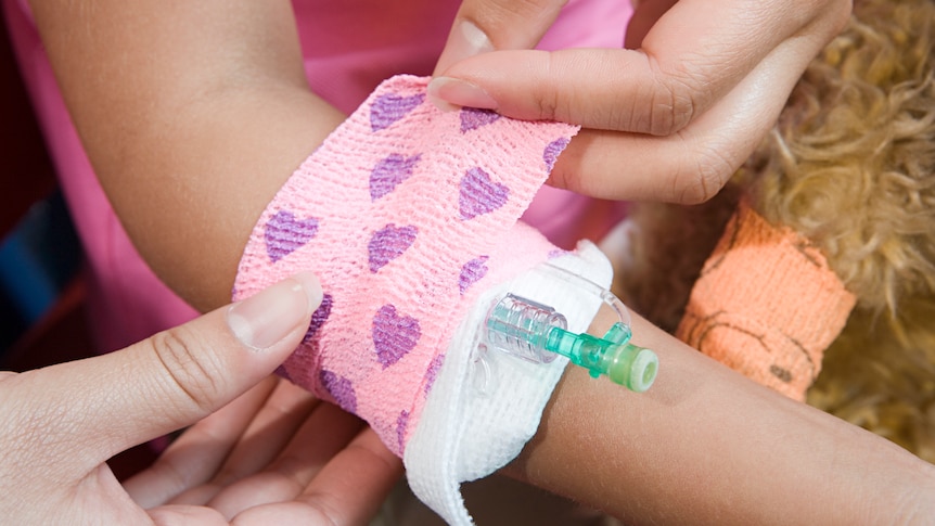 A girl has a bandage put around her catheter.