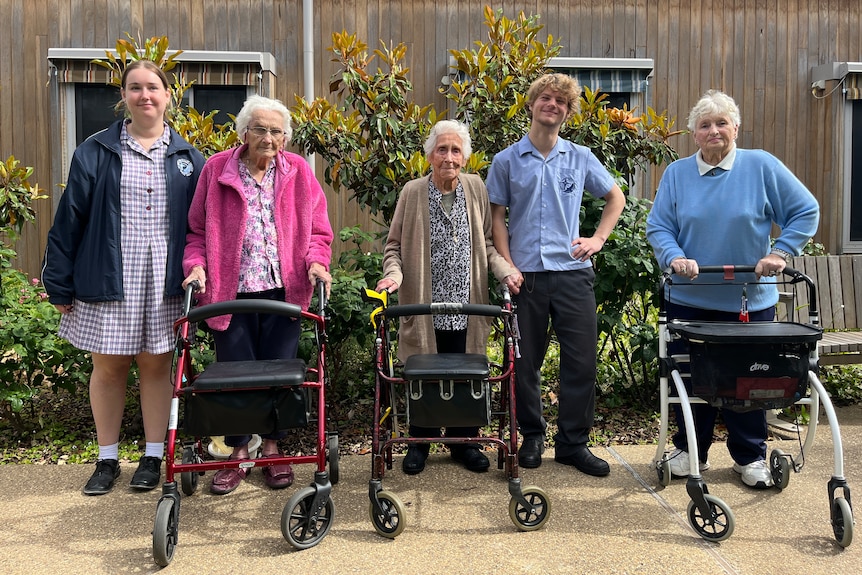 Two students stand with three aged care residents in a garden