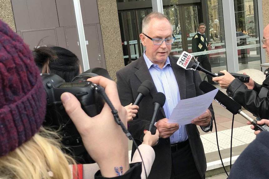 A man holds a piece of paper, surrounded by reporters