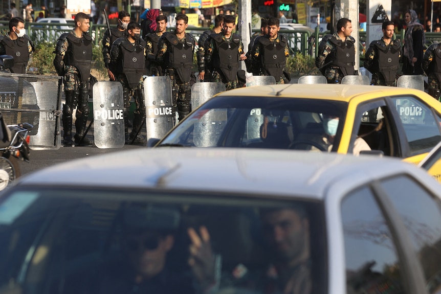 Iran's riot police forces stand in a street in Tehran as cars drive past.