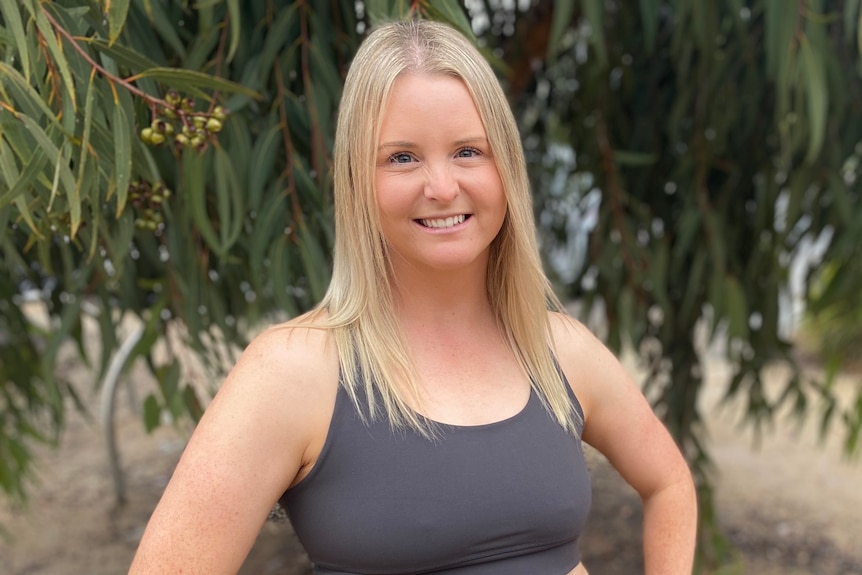 A photo of a woman in a sports bra with blonde hair standing under a tree 