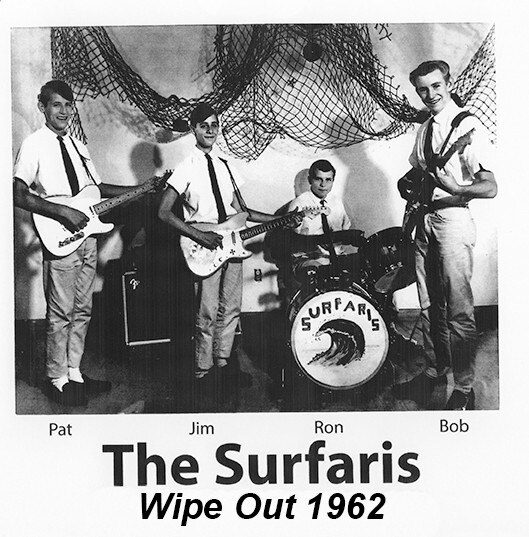 A group of four young men in shirts and ties, three holding guitars and one at a drum kit with the word 'Surfaris' on the front