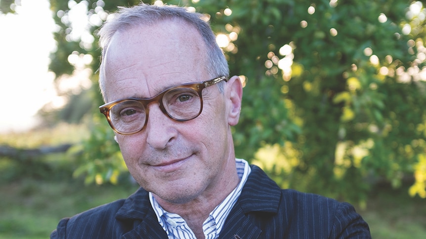 A close-up portrait of David Sedaris, trees in the background.