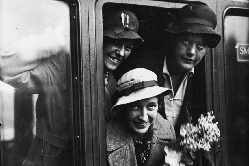 A black and white image of Betty Archdale with her head out of a train window holding flowers.