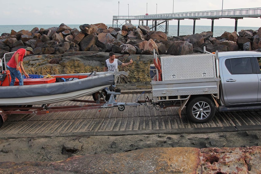 A photo of a ute backing a small boat down a boat ramp.