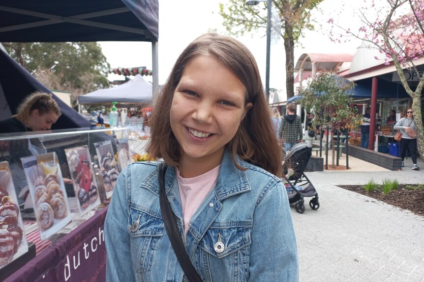 A young girl wearing a denim jacket smiles.
