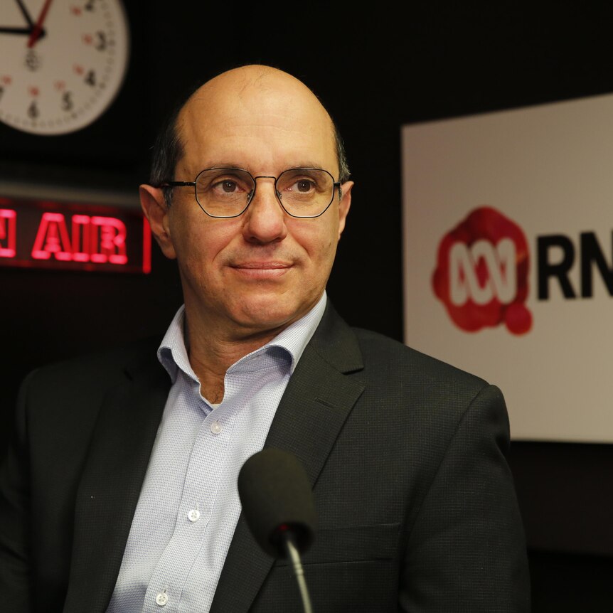  man with glasses in radio studio looks off into the distance , a slight smile on his lips