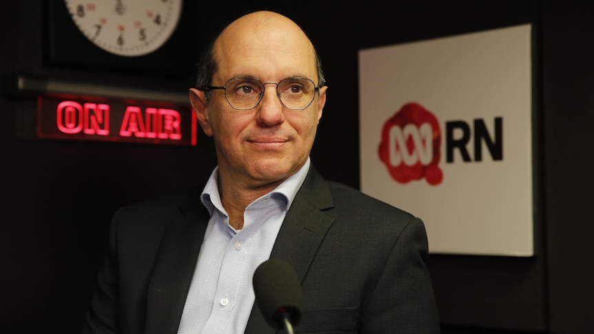  man with glasses in radio studio looks off into the distance , a slight smile on his lips