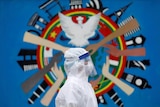 A person in white health PPE suit in front of a circular mural with painted hands and a white dove