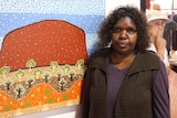 Senior Anangu leader Valerie Brumby stands in front of Indigenous artwork.