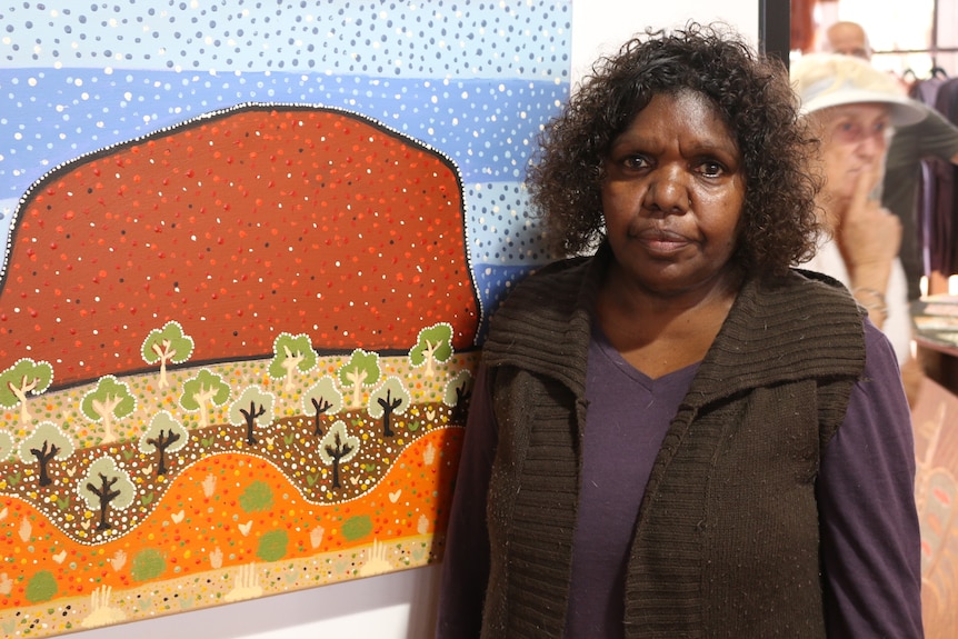 Senior Anangu leader Valerie Brumby stands in front of Indigenous artwork.