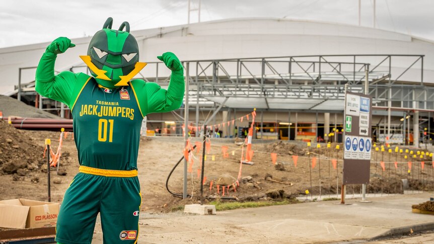 A person is dressed in a green ant mascot's uniform in front of a construction site. 
