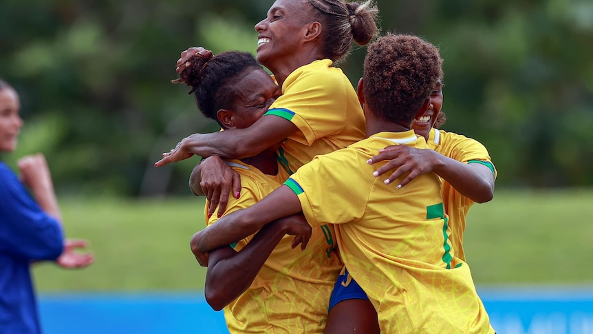 Solomon Islands football players in yellow jerseys hug as they celebrate beating Samoa in the OFC semi-final 