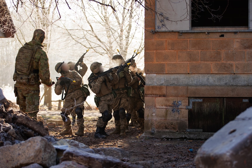 A group of several soldiers wield assault weapons next to a brick building in Europe