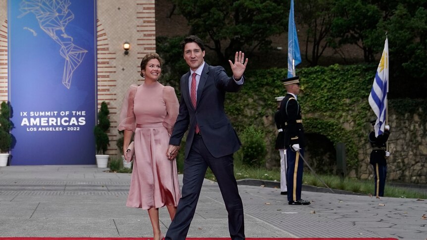 Justin Trudeau, wearing a black suit, holds Sophie Trudeau's hand. She is wearing a pink dress.