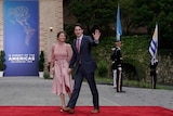 Justin Trudeau, wearing a black suit, holds Sophie Trudeau's hand. She is wearing a pink dress.