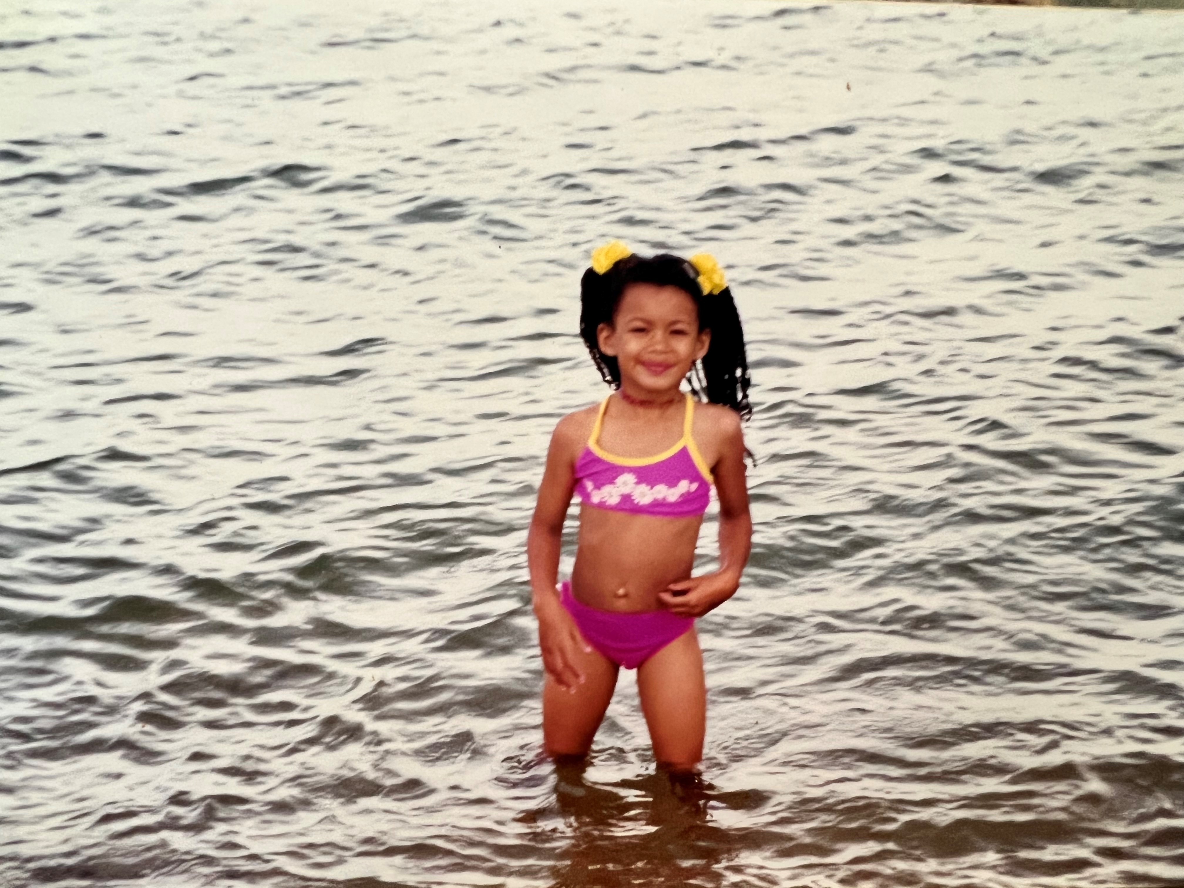 Yasmin stands in open water wearing a pink bikini. Her hair is braided and tied up in two pigtails with yellow ties.