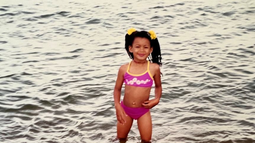 Yasmin stands in open water wearing a pink bikini. Her hair is braided and tied up in two pigtails with yellow ties.