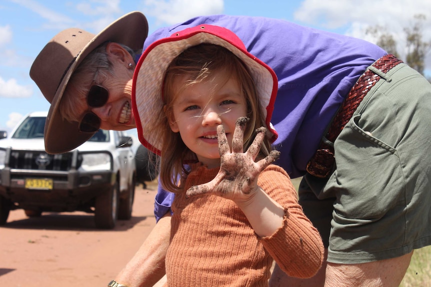 A little girl smiles while showing off her muddy fingers; her grandmother smiles and looks at her