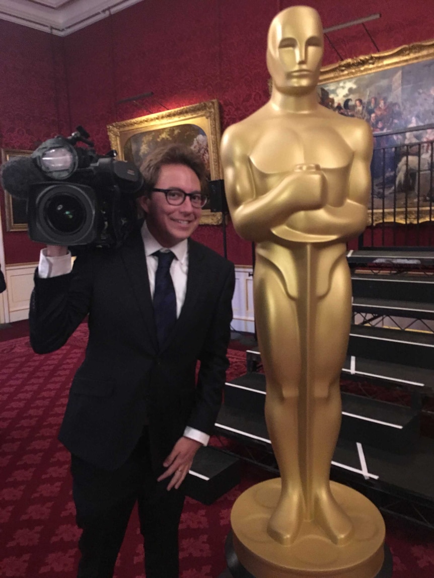 A cameraman stands next to a life-sized Oscar statue on the red carpet
