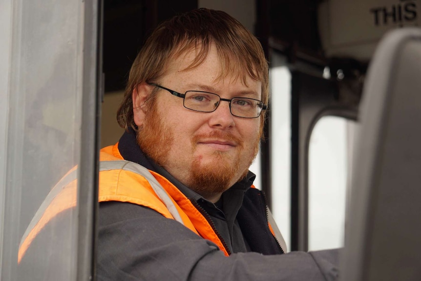 A tight head and shoulders shot of Davo Hunter sitting in the driver's seat of a bus looking at the camera.