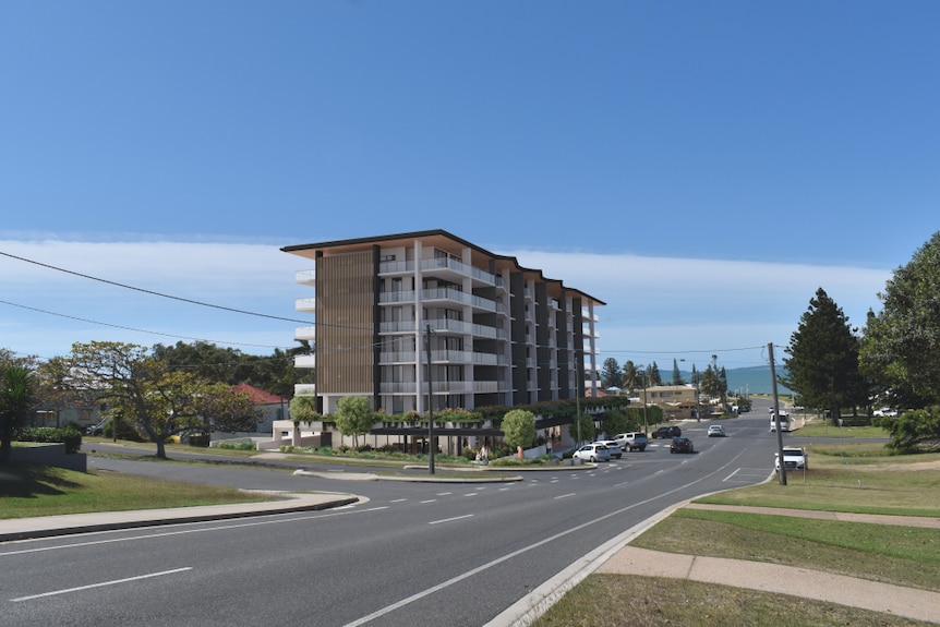 A beachside town with wide streets which are mostly empty. A 3D render of a seven-storey apartment sits in the centre. 