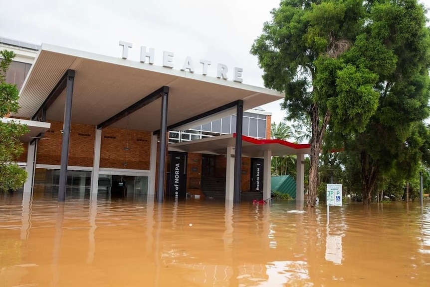 A building is partially submerged in muddy brown water. A roof bearing the word theatre stands above the water level.