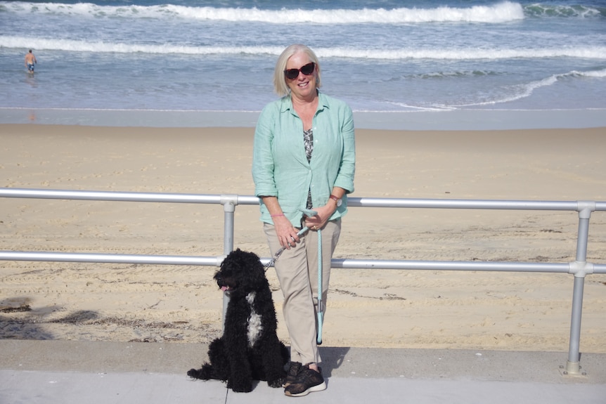 Une femme promène son caniche noir près de la plage.