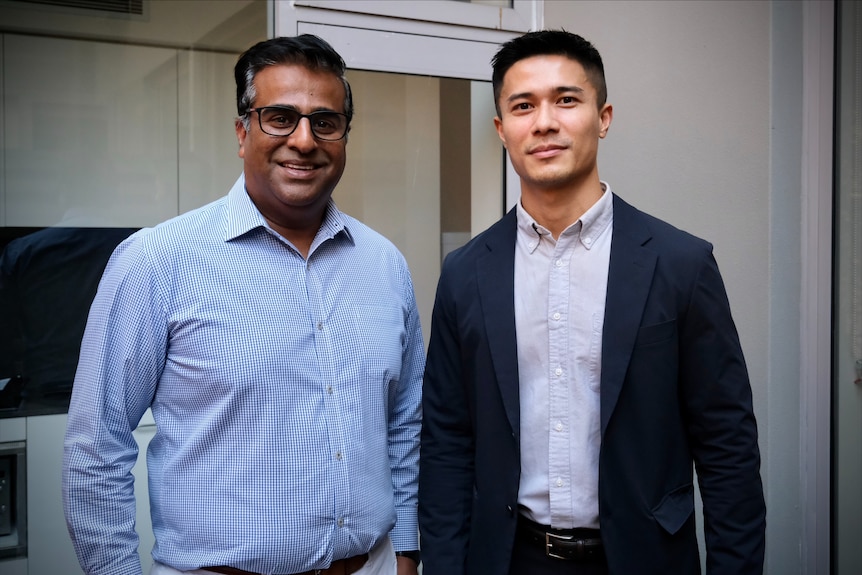 Two men wearing professional collared shirts without ties in an apartment building smiling.