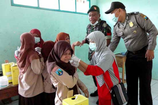 Two children in headscarves getting their vaccine shots with police observing