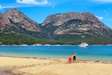 A scenic shot of a beach with mountains in the background and two children playing.