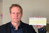 A man holding up a Commonwealth Bank cheque.