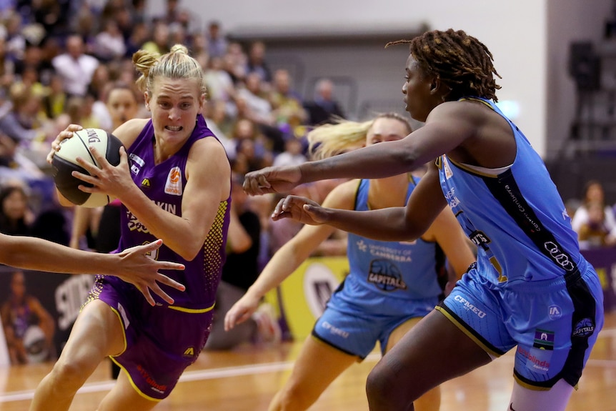 Kristy Wallace holds the ball as she approaches defenders during a WNBL game