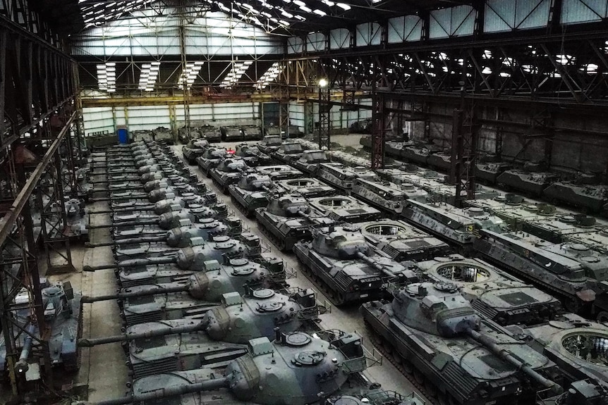 A line of green and black tanks stacked in a hanger.