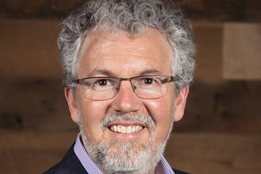 A close-up shot of a man with grey, curly hair and grey beard smiling.