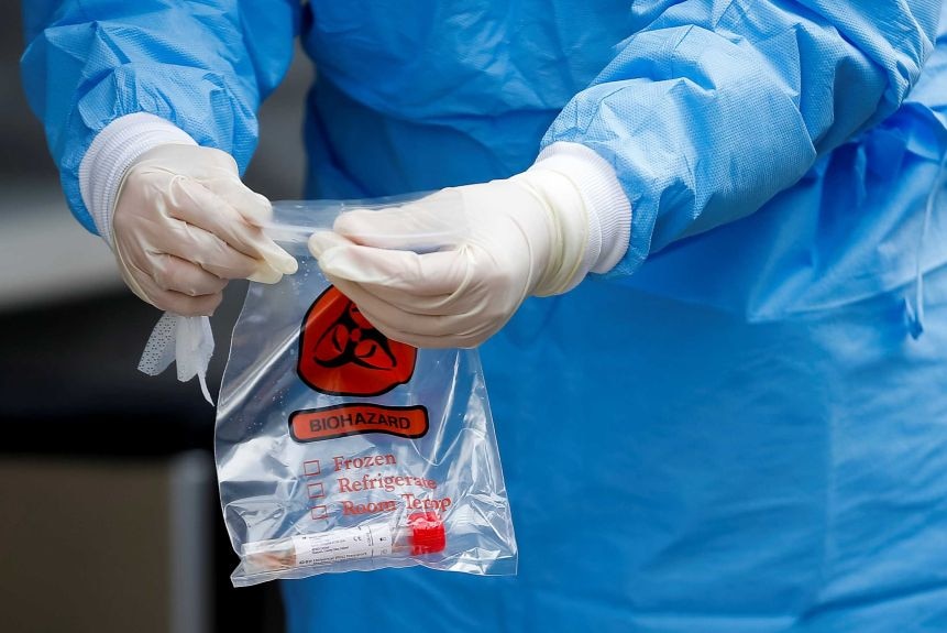 A man with gloves holds a blood test in a plastic bag.